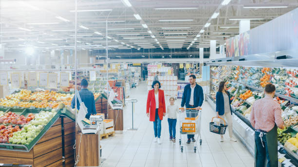 At the Supermarket: Happy Family of Three, Holding Hands, Walks Through Fresh Produce Section of the Store. Father, Mother and Daughter Having Fun Time Shopping. High Angle Panoramic Shot. At the Supermarket: Happy Family of Three, Holding Hands, Walks Through Fresh Produce Section of the Store. Father, Mother and Daughter Having Fun Time Shopping. High Angle Panoramic Shot. produce section stock pictures, royalty-free photos & images