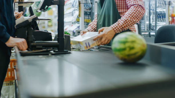 в супермаркете: выезд встречные руки кассира сканирует продукты питания, фрукты и другие товары здорового питания. чистый современный торг - cash register checkout counter customer shopping стоковые фото и изображения