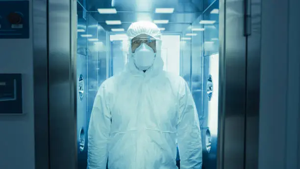 Scientist / Virologist / Factory Worker in Coverall Suit Disinfects Himself in Decontamination Shower Chamber. Biohazard Emergency Response.