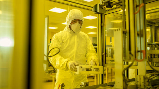 istock In the Manufacturing Facility Scientist Wearing Sterile Protective Coverall Set's up / Programs Modern Industrial 3D Printer, High Precision Manufacture of Semiconductors under Process. Shot from Inside with Yellow Filter. 1087219788