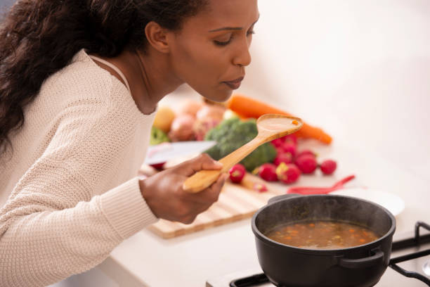 femme, dégustation de soupe avec une cuillère en bois dans la cuisine. - making soup photos et images de collection