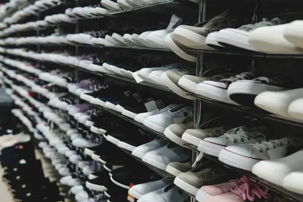 Photo of Side view of shoe store shelves with of lots of sneakers on sale. Low-budget comfortable footwear shopping. Unisex stylish teenager shoes. Rows of new runners in shoe shop. Stands of cheap trainers