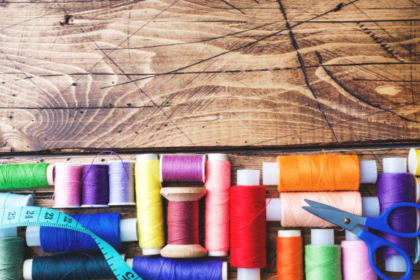 istock Colored spools of thread laid out in rows on wooden background. Copy space. 1087224272