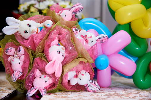 Bouquet of toys. Bouquet of cute stuffed rabbits on a background of balloons and flowers.