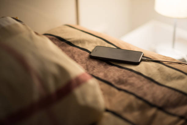 Smartphone is charging on bed Smartphone is charging on bed, risk of explosion of poor battery quality phone charger cable stock pictures, royalty-free photos & images