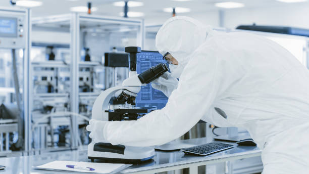 istock In Laboratory Scientist in Protective Clothes Doing Research Uses Microscope and Personal Computer. Modern Manufactory Producing Semiconductors and Pharmaceutical Items. 1087247430