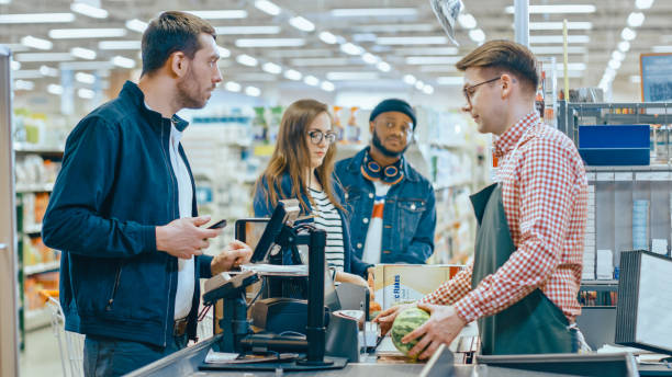 al supermercato: il cliente del banco di pagamento paga con lo smartphone per i suoi articoli. grande centro commerciale con cassiere amichevole, piccole linee e moderno sistema di terminali di pagamento wireless. - fare la fila foto e immagini stock