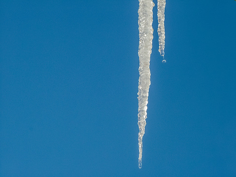 Icicles are melting in the sunlight against a blue sky. Close-up