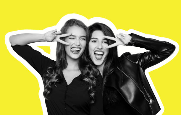 Two playful girls gesturing v-sign near eyes on yellow Magazine style collage of two foolish playful girls gesturing v-sign near winking eye, getting crazy at camera on yellow background funky photos stock pictures, royalty-free photos & images