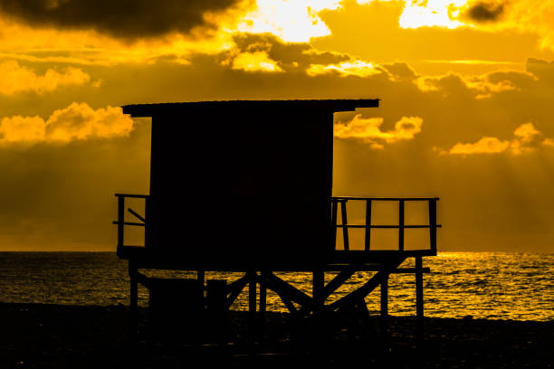美しい日没時に小さな木の家のシルエット - lifeguard orange nature beach ストックフォトと画像