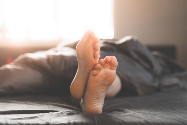 una donna è sdraiata a piedi nudi a letto in una mattinata di sole - bed human leg home interior comfortable foto e immagini stock