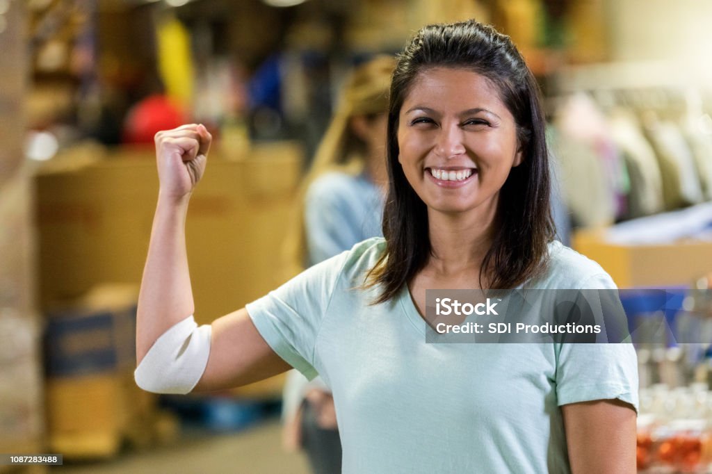 Woman flexes muscles after donating blood Confident mid adult Filipino woman flexes her arm after donating blood during charity event. She is smiling at the camera. Blood Donation Stock Photo