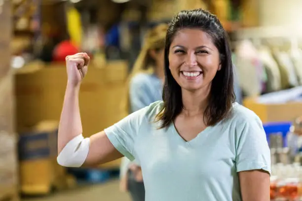 Confident mid adult Filipino woman flexes her arm after donating blood during charity event. She is smiling at the camera.