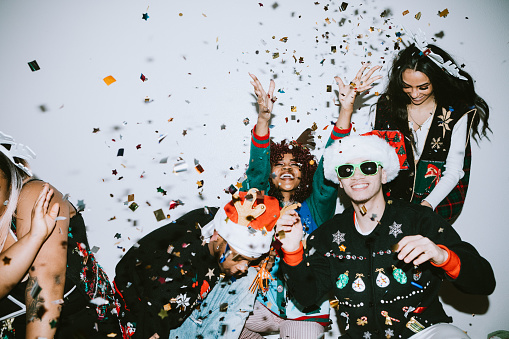 A group of young adult friends gather at a home for Christmas celebration over the holiday, dressed to fit the occasion with various Christmas accessories and ugly sweaters.  They pose for some photos, direct camera flash.