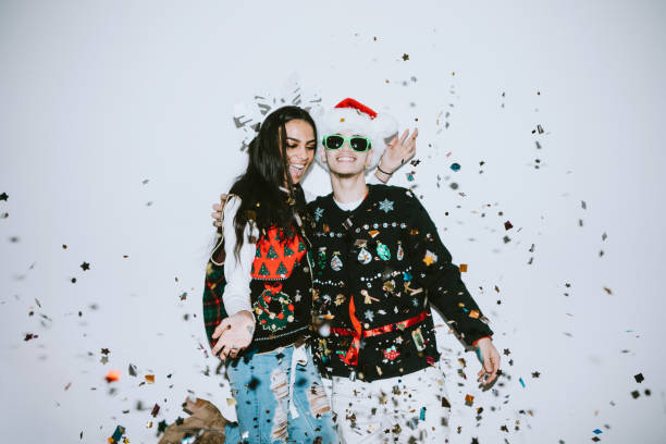 Generation Z Young Couple Celebrates With Confetti A young man and woman embrace in celebration as confetti falls on them.  Christmas or New Years festivities. Christmas outfit stock pictures, royalty-free photos & images