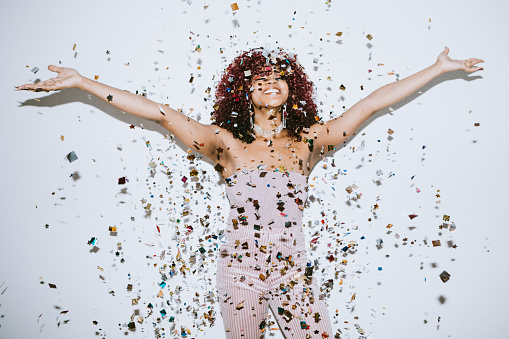 A young woman raises her hands in celebration as confetti falls on her.  Christmas or New Years festivities.
