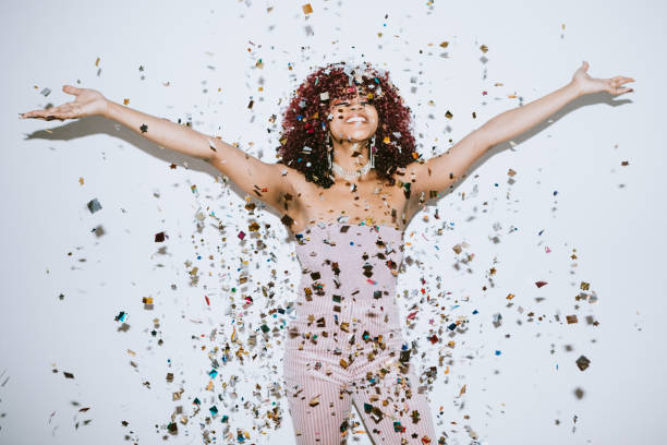 Generation Z Young Woman Celebrates With Confetti A young woman raises her hands in celebration as confetti falls on her.  Christmas or New Years festivities. new years eve parties stock pictures, royalty-free photos & images