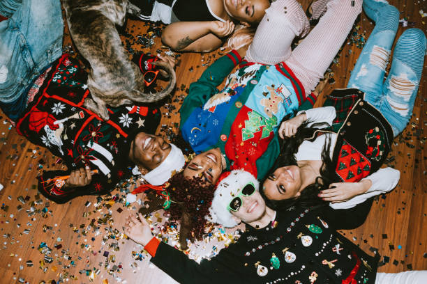 Generation Z Friends Christmas Party A group of young adult friends gather at a home for Christmas celebration over the holiday, dressed to fit the occasion with various Christmas accessories and ugly sweaters.  They relax on the floor, covered with confetti. ugly dog stock pictures, royalty-free photos & images