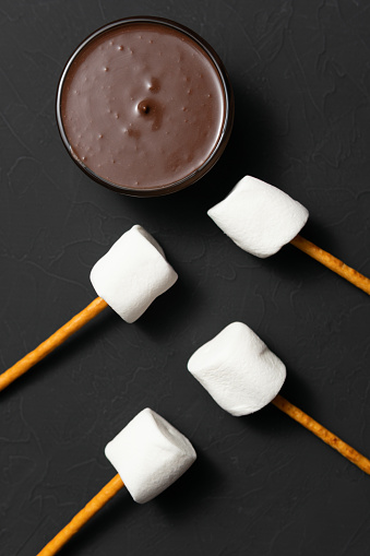 Top view of melted chocolate in a bowl with white fluffy marshmallows on sticks