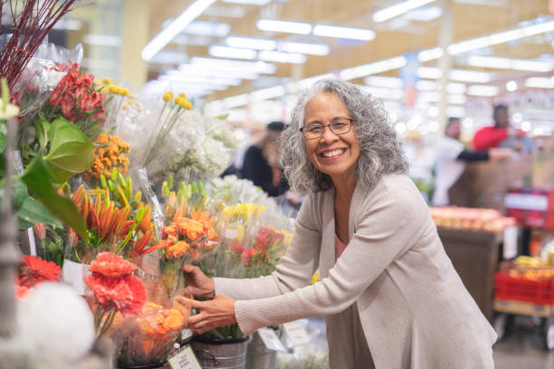 年配の女性が店で花をピックアップします。 - florist supermarket flower bouquet ストックフォトと画像