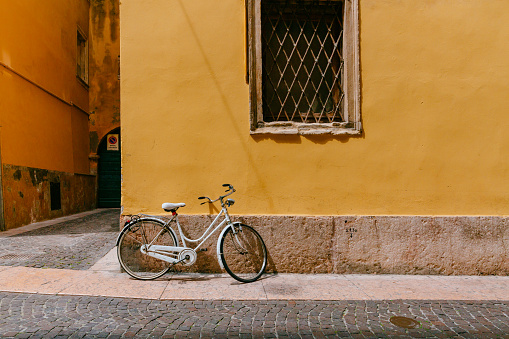 A white bike parked agaisnt yellow wall in the street of Verona, Italy