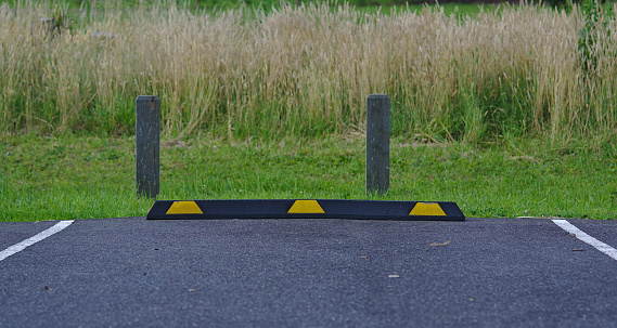 Rubber parking block in black and yellow colors on asphalt surface with wild grass background