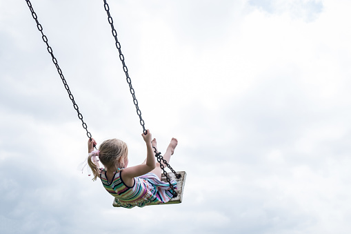 A little girl swings high on a wooden swing on a cloudy day.