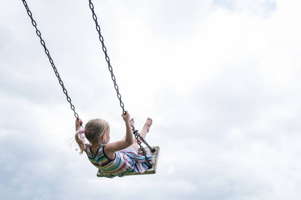 Little child swinging on a wooden swing A little girl swings high on a wooden swing on a cloudy day. swing stock pictures, royalty-free photos & images