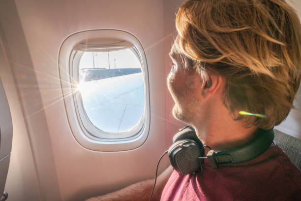istock Young man in airplane looking through window 1087432060