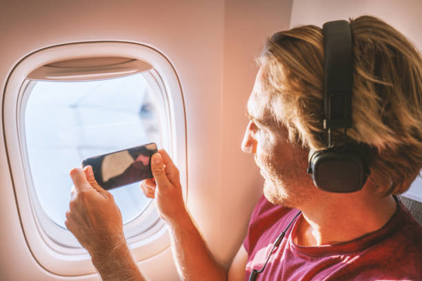 istock Young man in airplane using mobile phone during flight to take picture of view 1087441808
