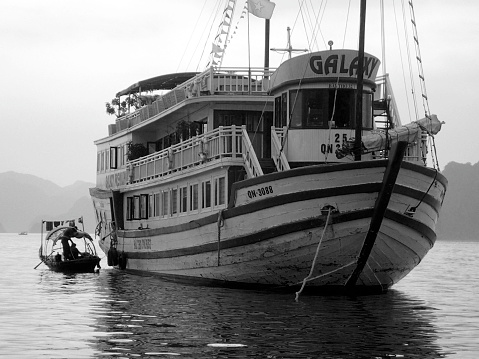 Halong Bay, Vietnam, 2018 april 25 : small boat selling goods to tourists in their cruise ship. Tourism influencing traditional life. black and white