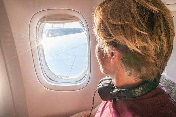 istock Young man in airplane looking through window 1087448544