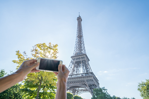 Pov of person taking mobile phone picture of the Eiffel Tower in Paris. People travel discovery city concept\nYoung caucasian woman tourist in Paris