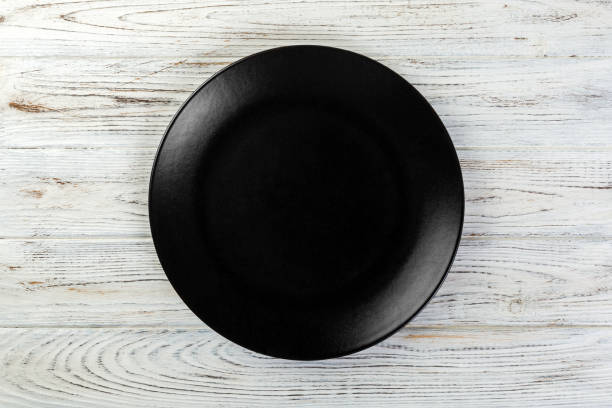 istock Directy above Empty black matte plate on white wooden background 1087462590