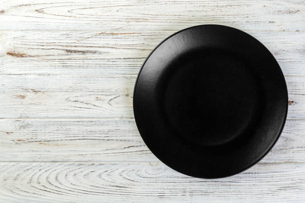 istock Directy above Empty black matte plate on white wooden background with copy space 1087462708