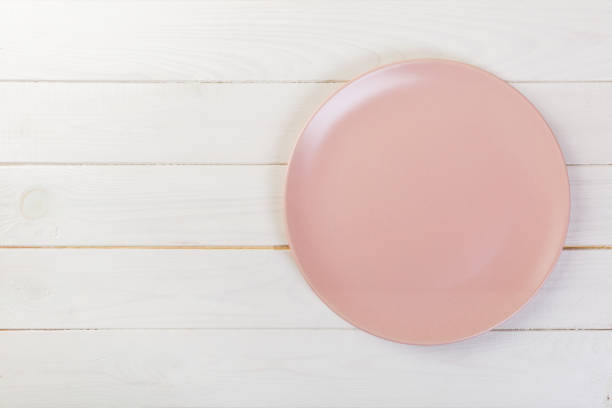 istock Directy above Empty pink matte plate on white wooden background with copy space 1087464346