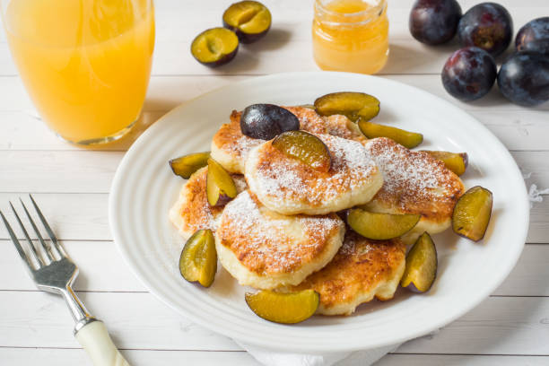 Cheese pancakes in powdered sugar with fresh plums on a plate.