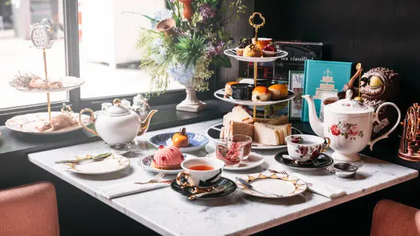 English afternoon tea set including hot tea, pastry, scones, sandwiches and mini pies on marble top table.