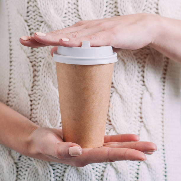 A woman in a white sweater holding a paper Cup of coffee. Template for text or design