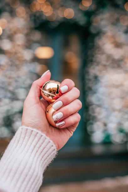 Christmas inspired manicure Closeup photo of a beautiful female hand with nude Christmas inspired manicure holding gold bells. christmas nails stock pictures, royalty-free photos & images