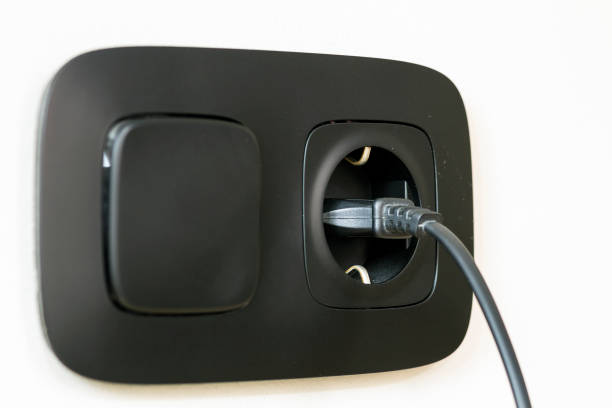 istock Black power cord cable plugged into european wall outlet on white plaster wall 1087494110