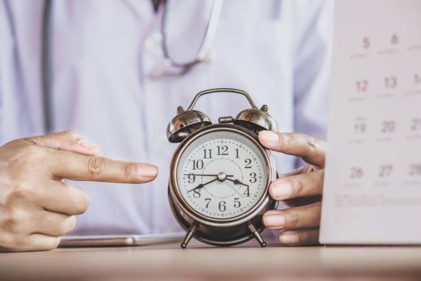 doctor hand holding alarm clock showing the time - appointment reminder doctor calendar imagens e fotografias de stock