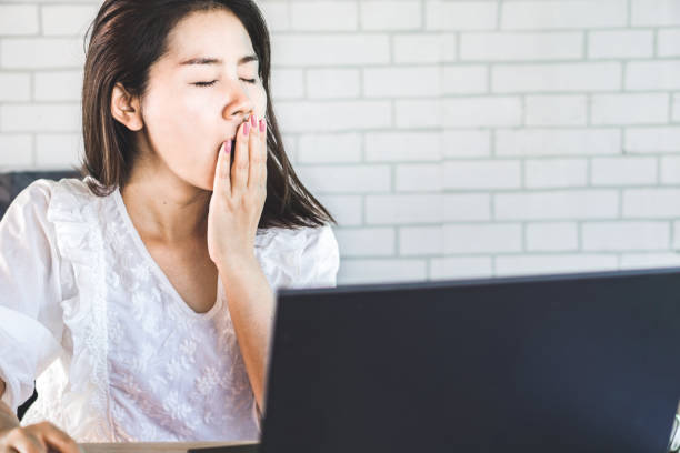 istock tired Asian woman yawning while working at workplace 1087502676