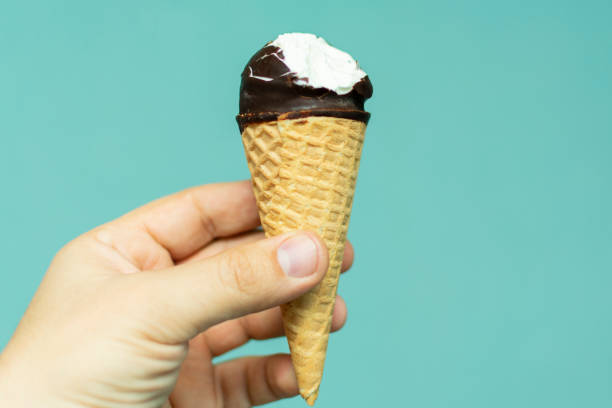 istock bitten vanilla ice cream in a cone and in chocolate icing on a blue background in hand 1087533984