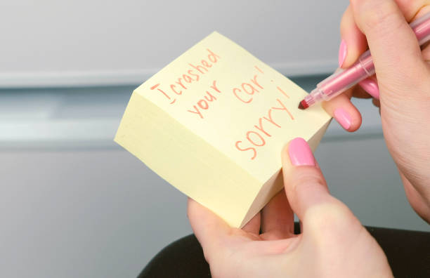 istock Closeup woman's hands write on yellow sticker paper sheets words i crashed your car sorry. 1087534816