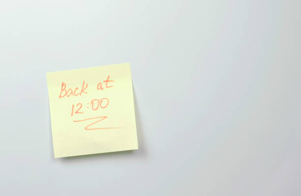 istock Yellow sticker paper sheet with words back at 12 on a white board 1087536040