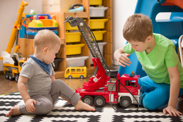 frères et sœurs jeunes garçons jouant avec un jouet incendie camion dans la chambre d’enfant. enfants qui jouent les voitures dans leur chambre. activités de loisirs à la maison. aire de jeux. à l’intérieur. profession. pompier. - playground cute baby blue photos et images de collection