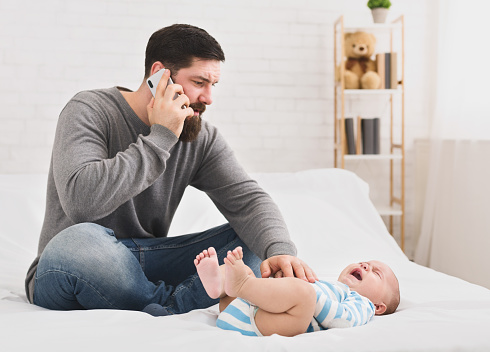Little baby suffering from colic, worried dad massaging his belly and calling to doctor, copy space