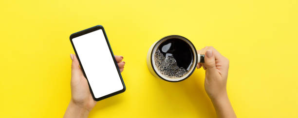 femininas mãos segurando um celular preto com tela branca em branco e a caneca de café. imagem da maquete com espaço de cópia para design. bandeira de vista superior, sobre fundo amarelo, liso leigo - text messaging mobile phone teenagers only people - fotografias e filmes do acervo