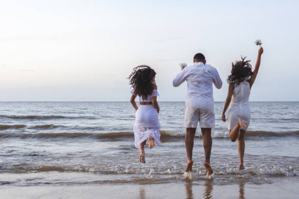 Happy friends celebrating reveillon on the beach, running to the sea and jumping waves. Paraiso beach, Mosqueiro Happy friends celebrating reveillon on the beach, running to the sea and jumping waves. They wear white clothes. Group of young people enjoying and partying together. Happiness, togetherness, youth and new year's eve concepts. Paraiso beach, Mosqueiro wave jumping stock pictures, royalty-free photos & images